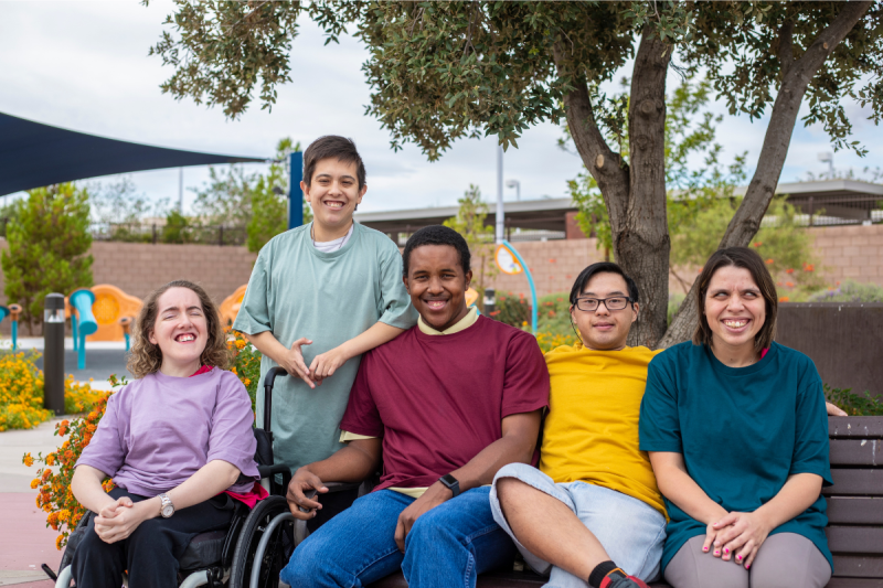 An adult wheelchair user and a colleague smiling while looking at a laptop together