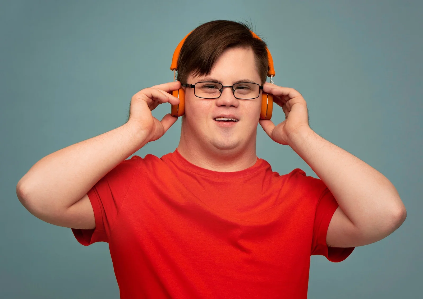 A smiling young man in a red shirt adjusting orange headphones